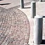 Plain bollards mounted in concrete forming a curve adjacent to a highly decorative curved paver design